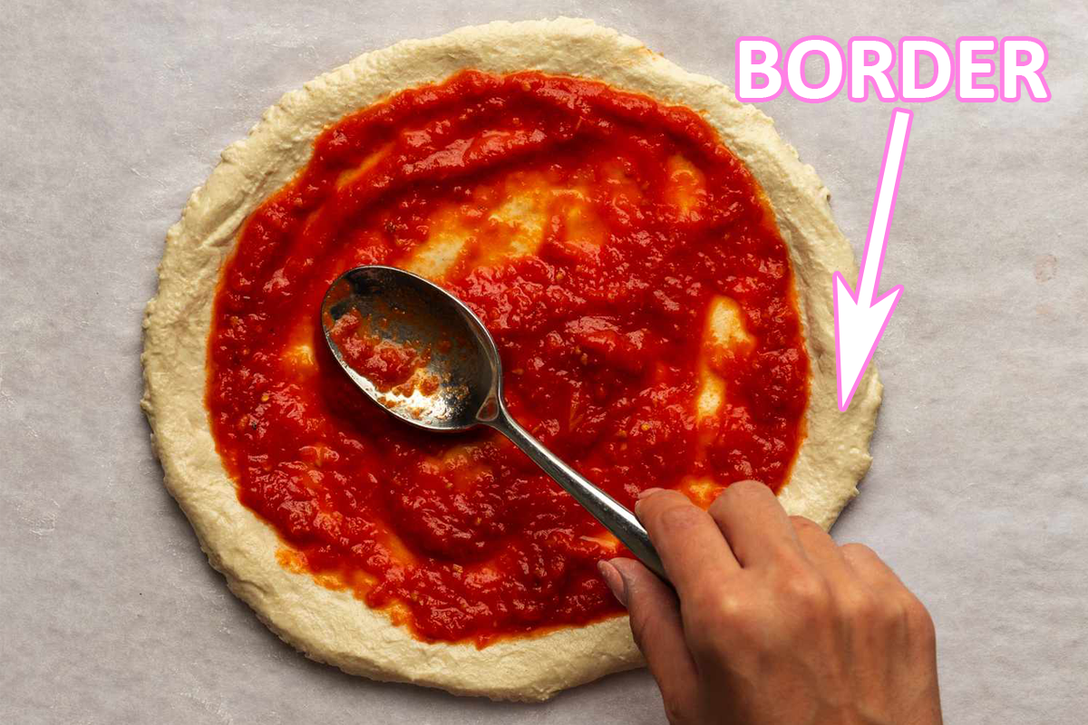 A pizza base with sauce being spread on